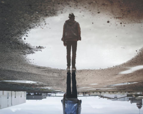 A man's reflection in a puddle shows him standing tall.