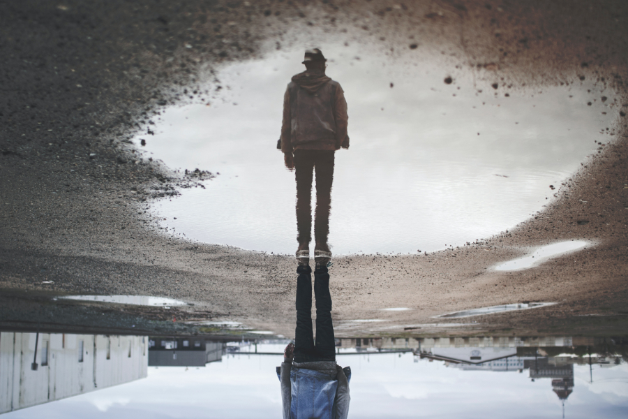 A man's reflection in a puddle shows him standing tall.