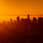 A city skyline is bathed in an orange sunset.