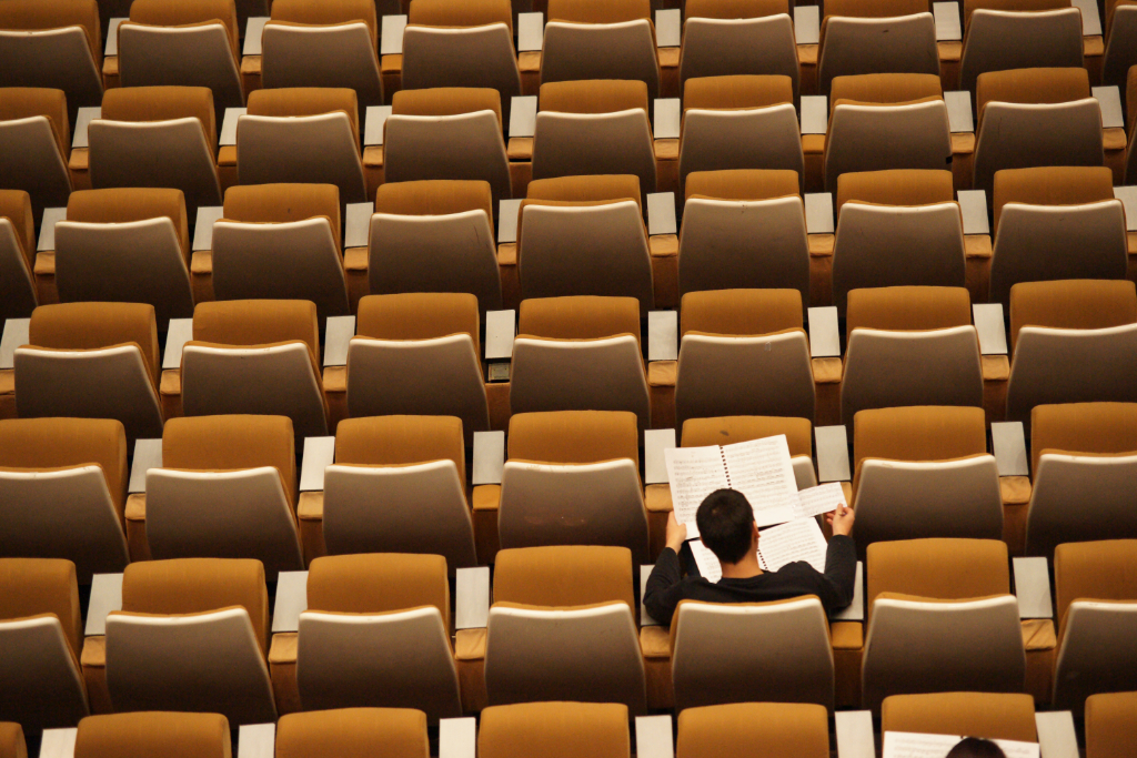 A university student reads his notes in an otherwise empty lecture hall.