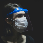 A nurse looks to the side, covered in a mask and shield over their eyes.