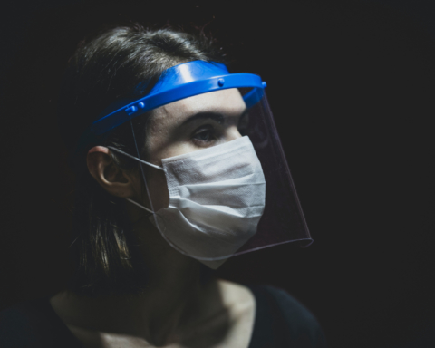 A nurse looks to the side, covered in a mask and shield over their eyes.