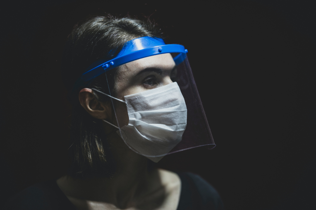 A nurse looks to the side, covered in a mask and shield over their eyes.