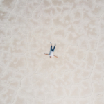 An aerial shot of a man lying alone on a vast salt flat.