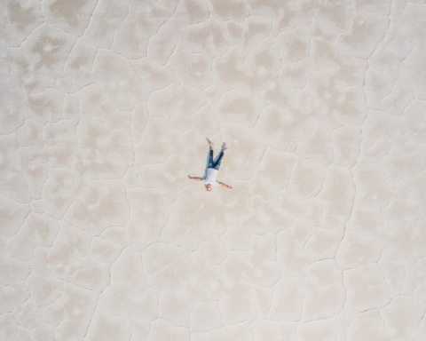 An aerial shot of a man lying alone on a vast salt flat.