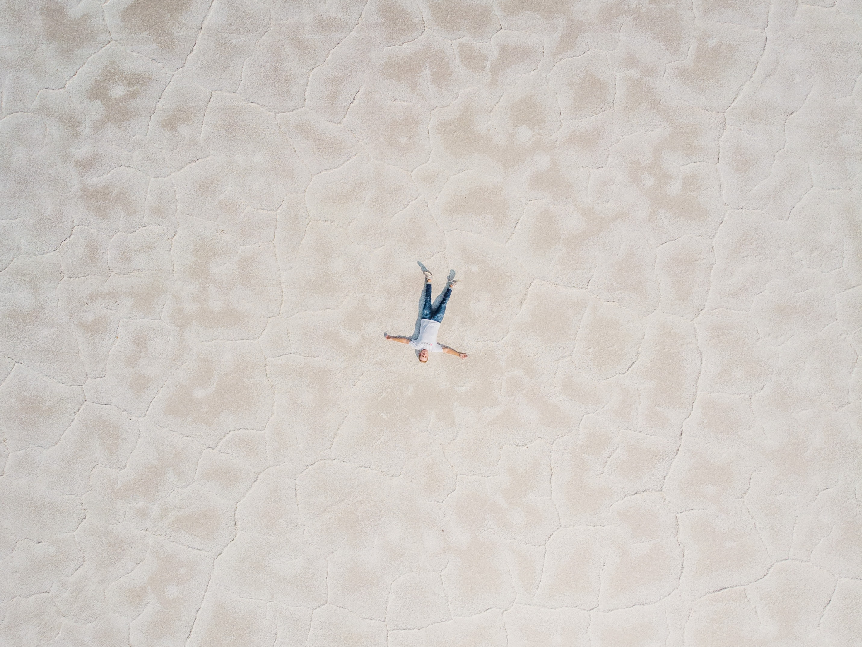 An aerial shot of a man lying alone on a vast salt flat.