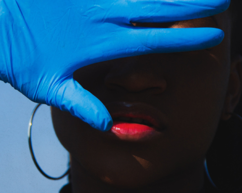 A hand covered in a blue medical glove is raised over a Black person's face.