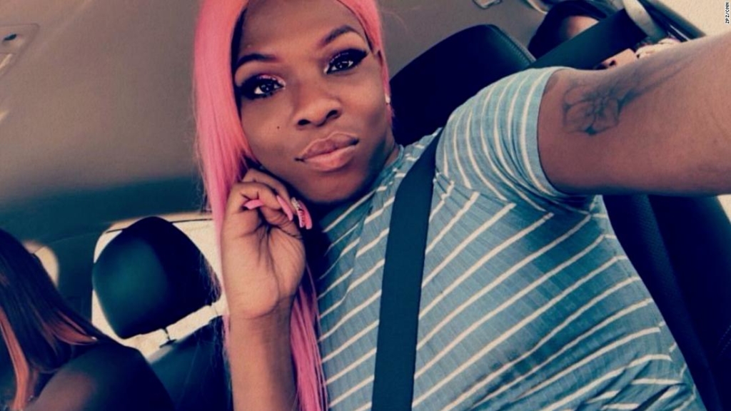 A photograph of Muhlaysia Booker, a Black woman with pink hair and a blue and white shirt in her car.