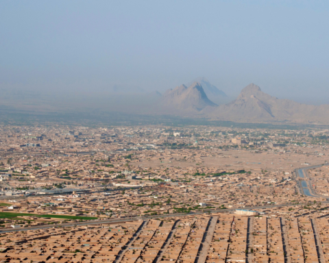 An aerial photo of Kandahar Province, Afghanistan in 2013. The red clay of the buildings match the reddish mountains in the background.