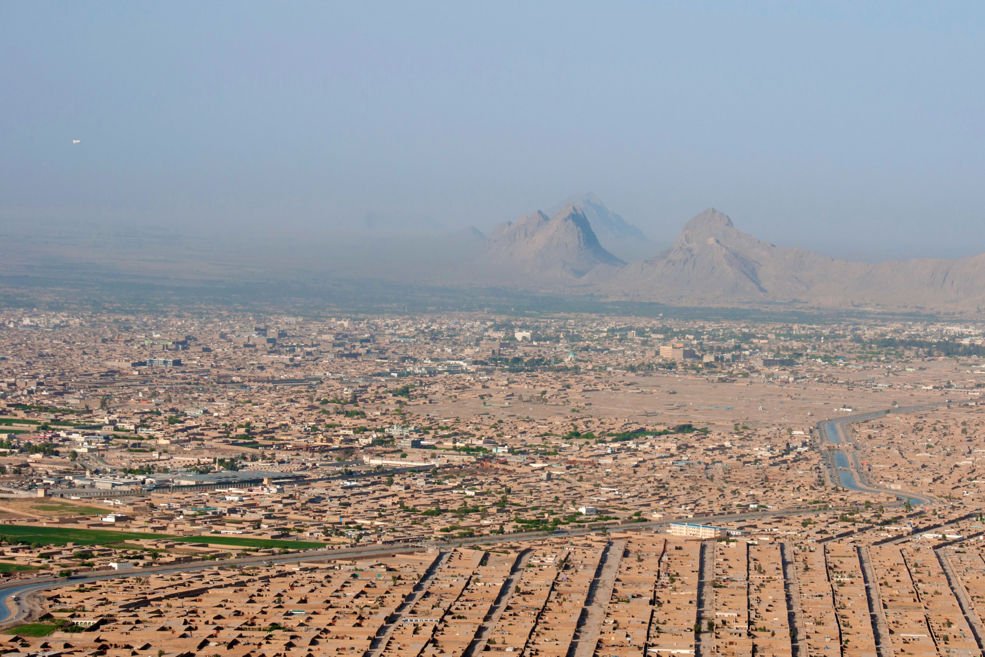 An aerial photo of Kandahar Province, Afghanistan in 2013. The red clay of the buildings match the reddish mountains in the background.