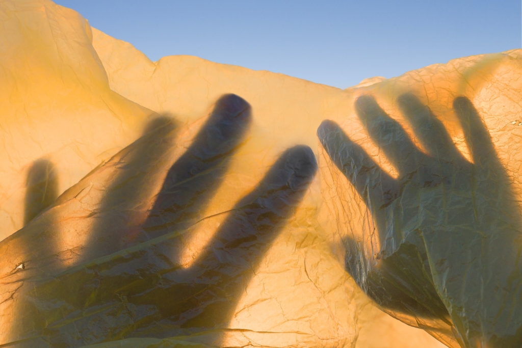 This photograph, with its blue sky and yellow sand, reminds the reader of the Ukrainian flag and a beautiful valley. Superimposed over that is a shadow of two hands.