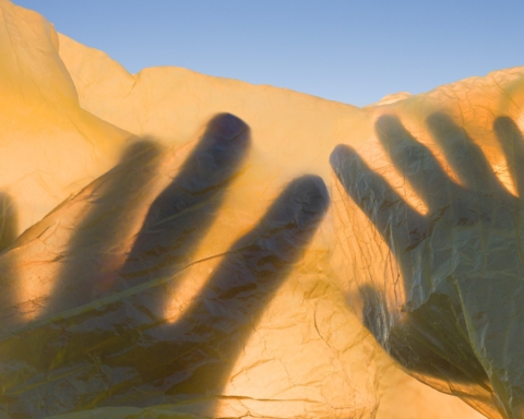 This photograph, with its blue sky and yellow sand, reminds the reader of the Ukrainian flag and a beautiful valley. Superimposed over that is a shadow of two hands.