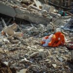 A photograph of an orange elephant doll amidst a pile of concrete rubble.