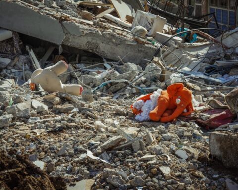 A photograph of an orange elephant doll amidst a pile of concrete rubble.