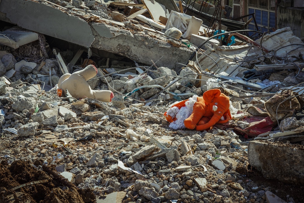 A photograph of an orange elephant doll amidst a pile of concrete rubble.