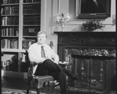 A photograph of Jimmy Carter in the white house, seated on a chair in front of a portrait of George Washington.