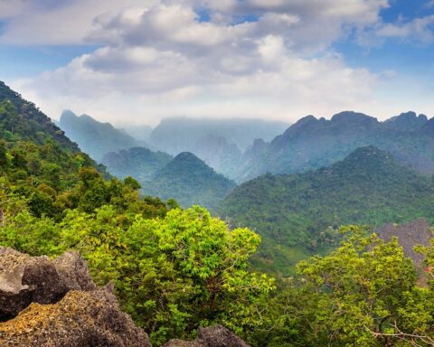 A Laotian mountain-side covered in verdure below a sky full of light clouds.